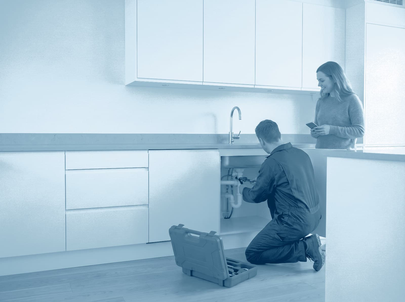 Un fontanero trabaja bajo el fregadero de la cocina mientras la inquilina mira